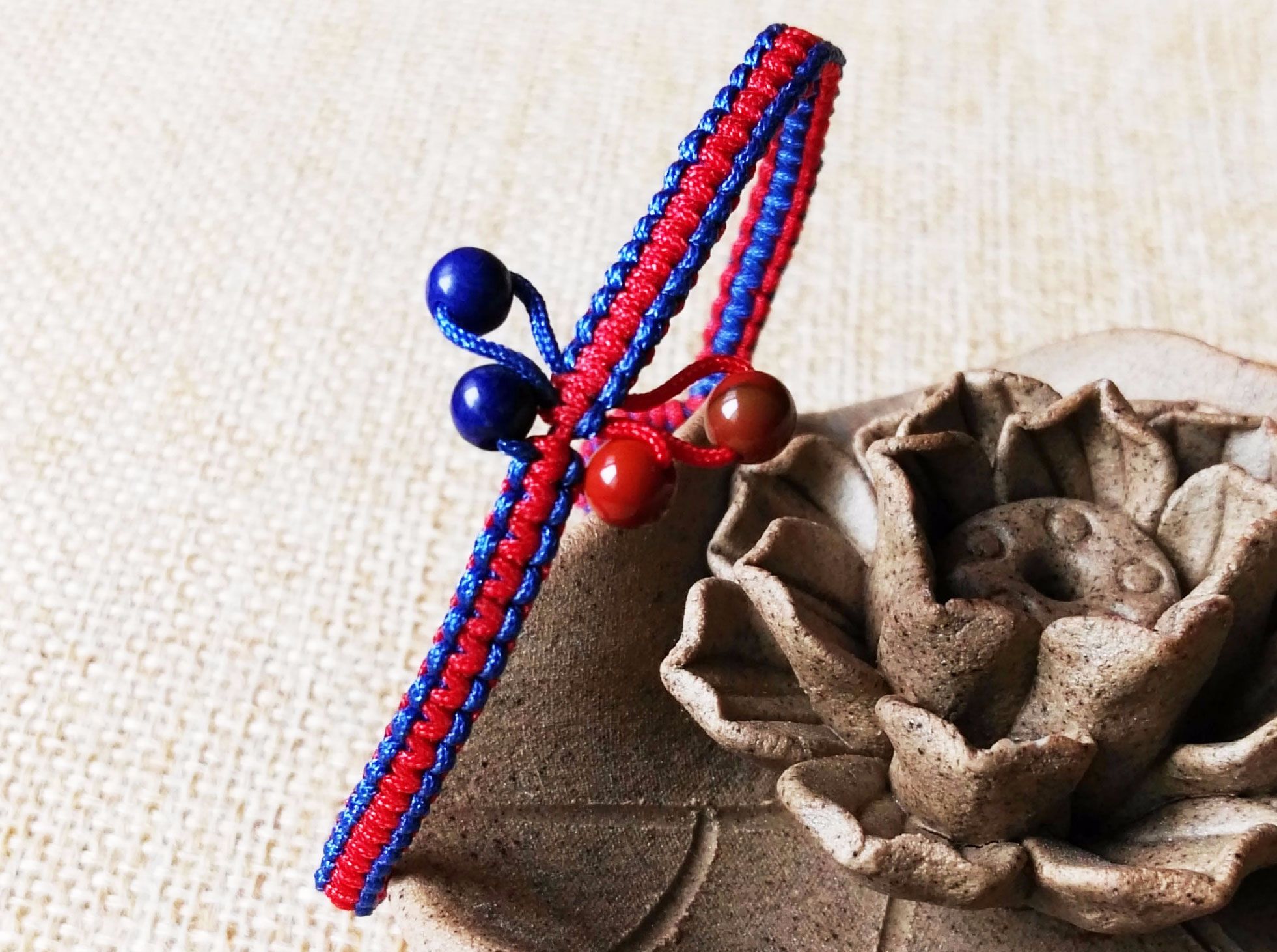 制作一个蝴蝶花手圈，整个手圈用到“两色两结”，两色是指（红色+蓝色），两结是指（平结+金刚结），圆珠材质是（青金石+战国红）